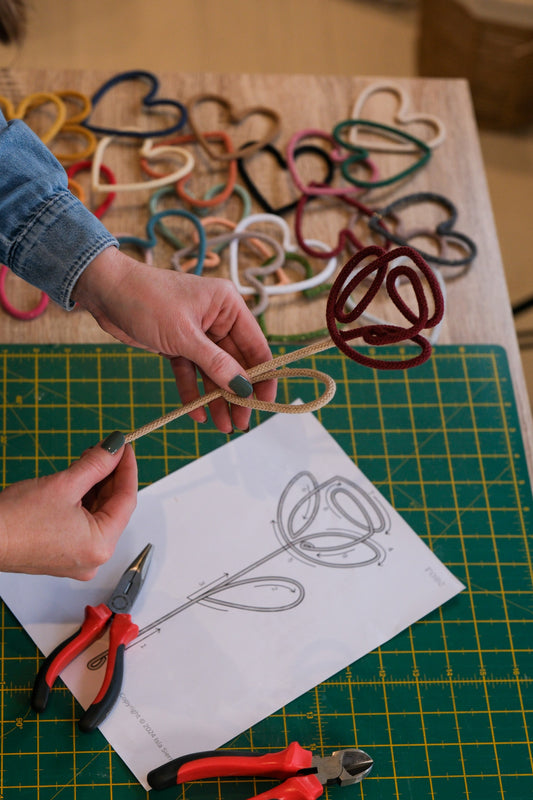 Person crafting wire heart shapes on a cutting mat with pliers.