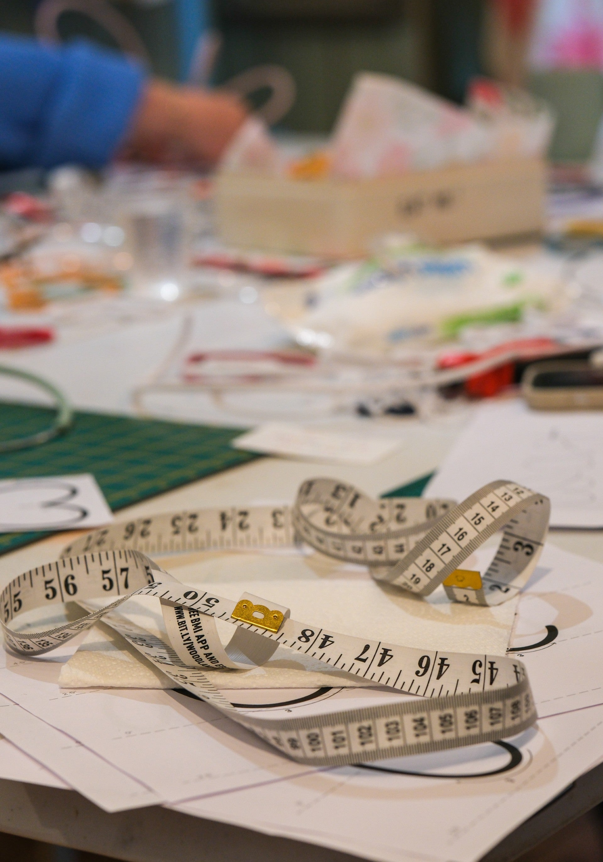 Measuring tape on a table with craft materials in the background for creative workshop