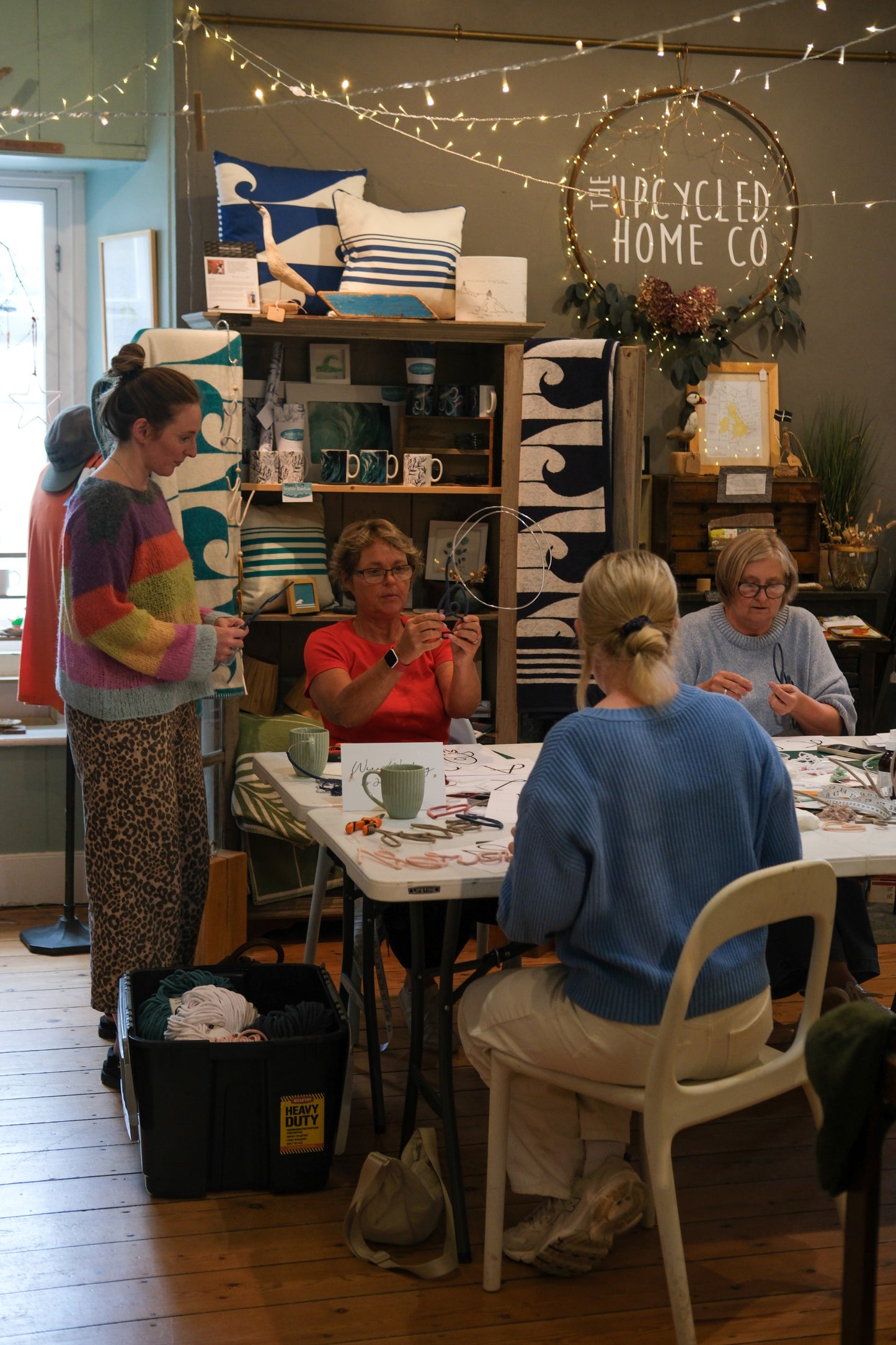 People gathered around a craft table in a room with 'The Recycled Home Co' branding.