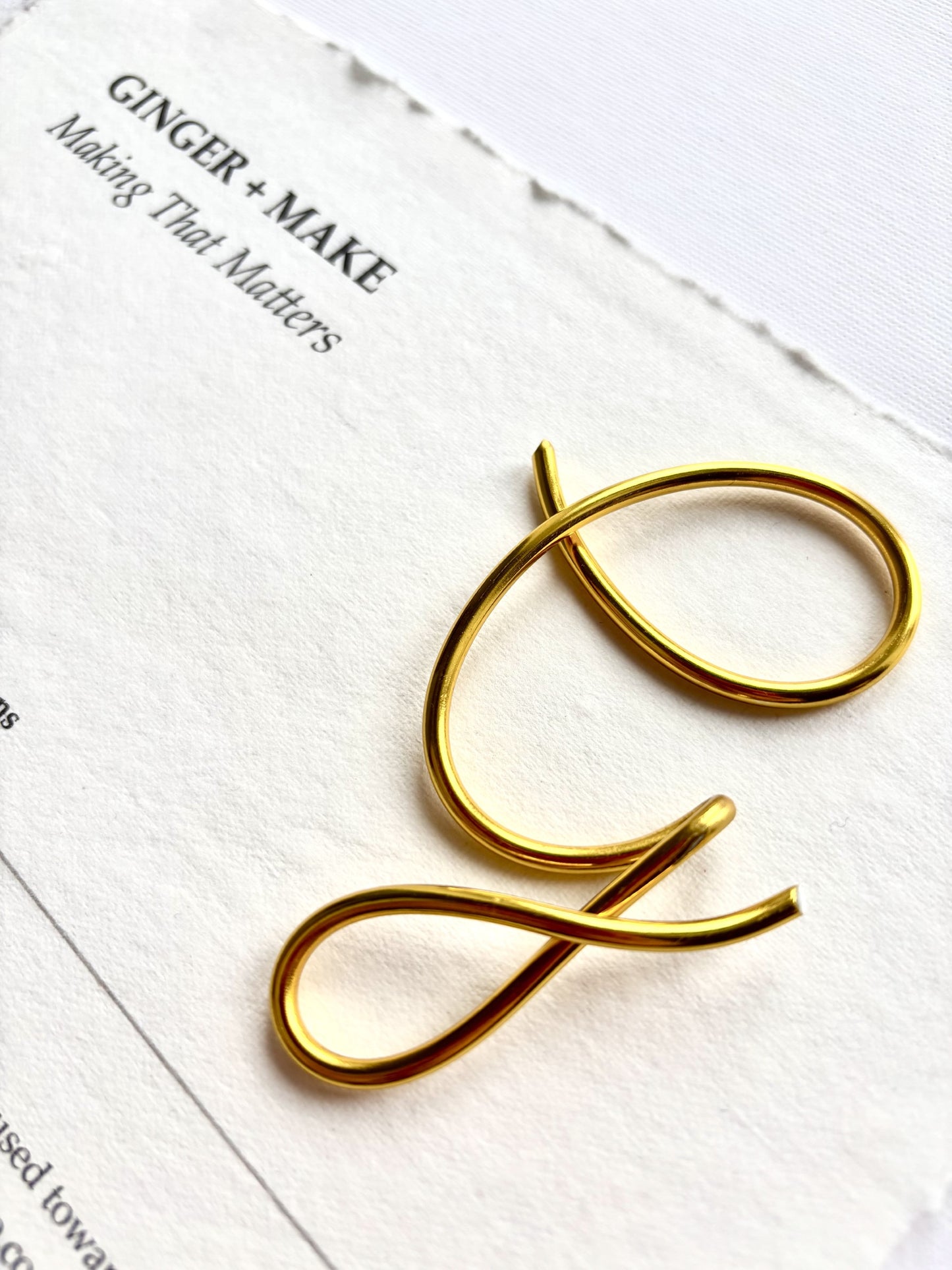 A gold metal letter 'G' sign or decorative letter piece resting on textured white paper with printed text in the background.