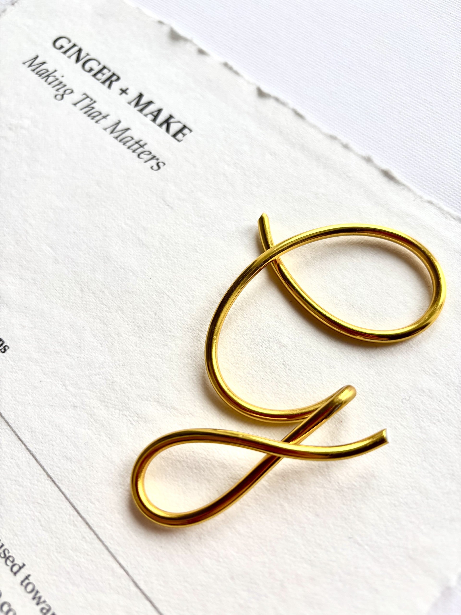 A gold metal letter 'G' sign or decorative letter piece resting on textured white paper with printed text in the background.