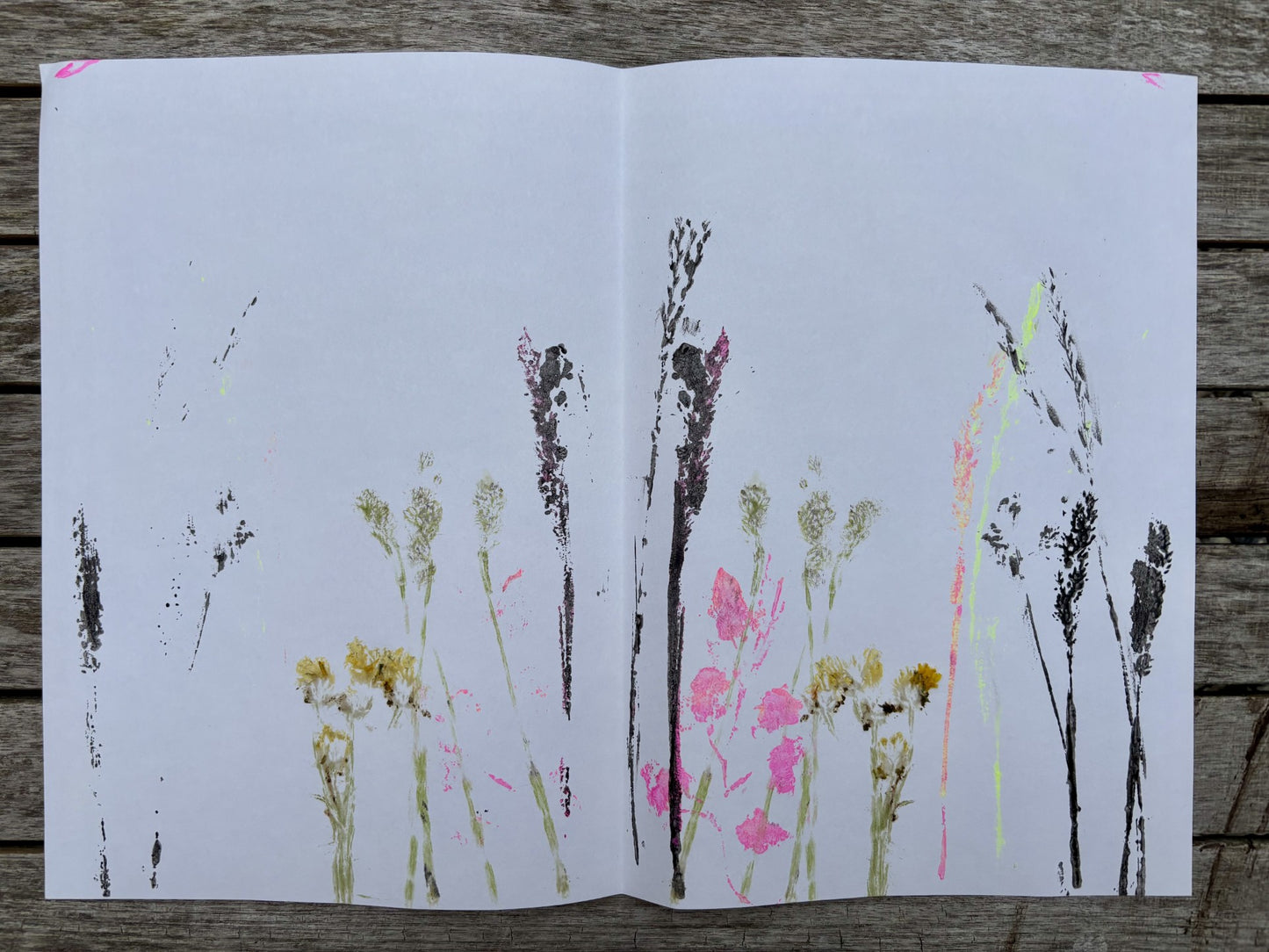 Prints of flowers and plants on a white sheet of paper with black ink smudges, placed on a wooden surface.