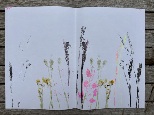 Prints of flowers and plants on a white sheet of paper with black ink smudges, placed on a wooden surface.