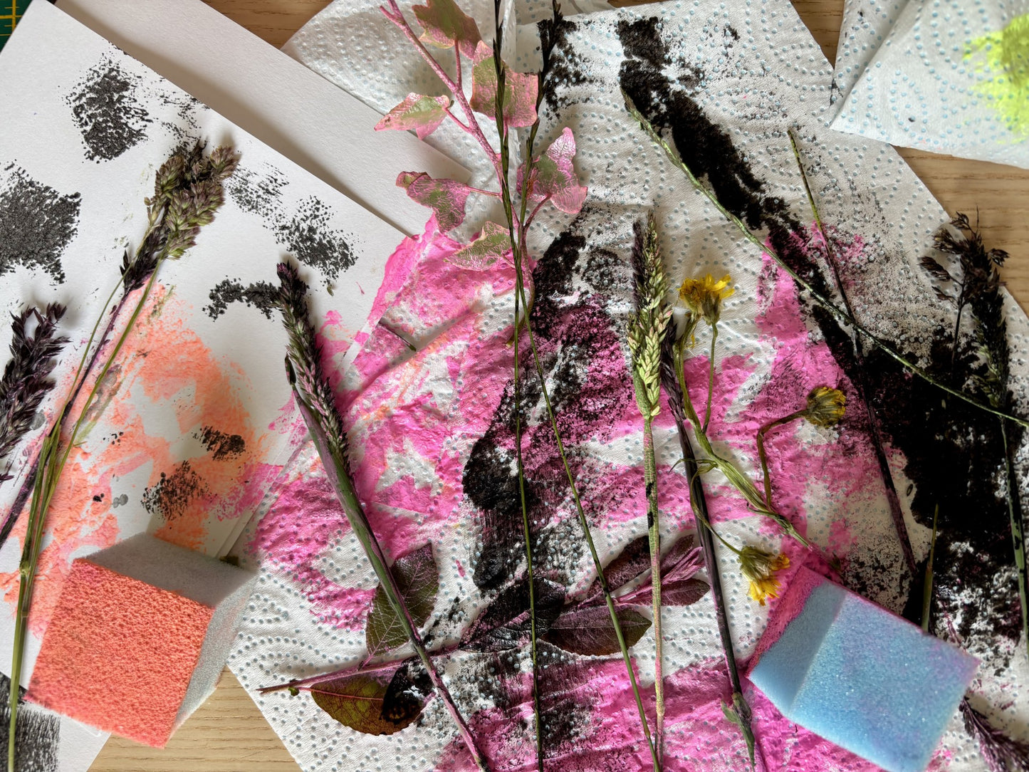 Artistic arrangement of dried plants and flowers on a textured surface with pink and black abstract patterns.