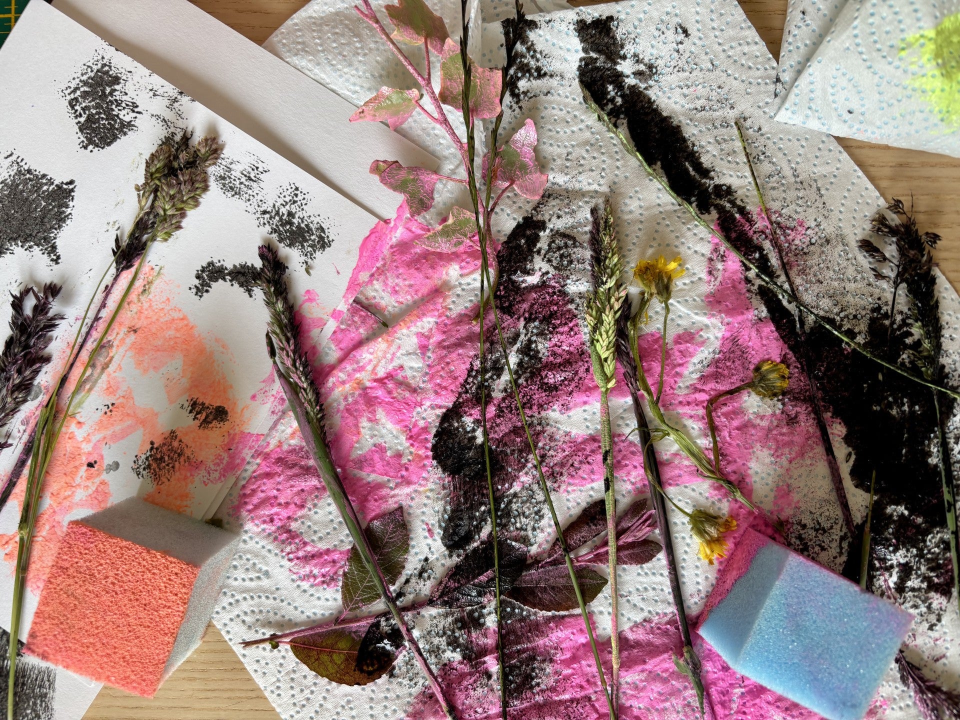 Artistic arrangement of dried plants and flowers on a textured surface with pink and black abstract patterns.
