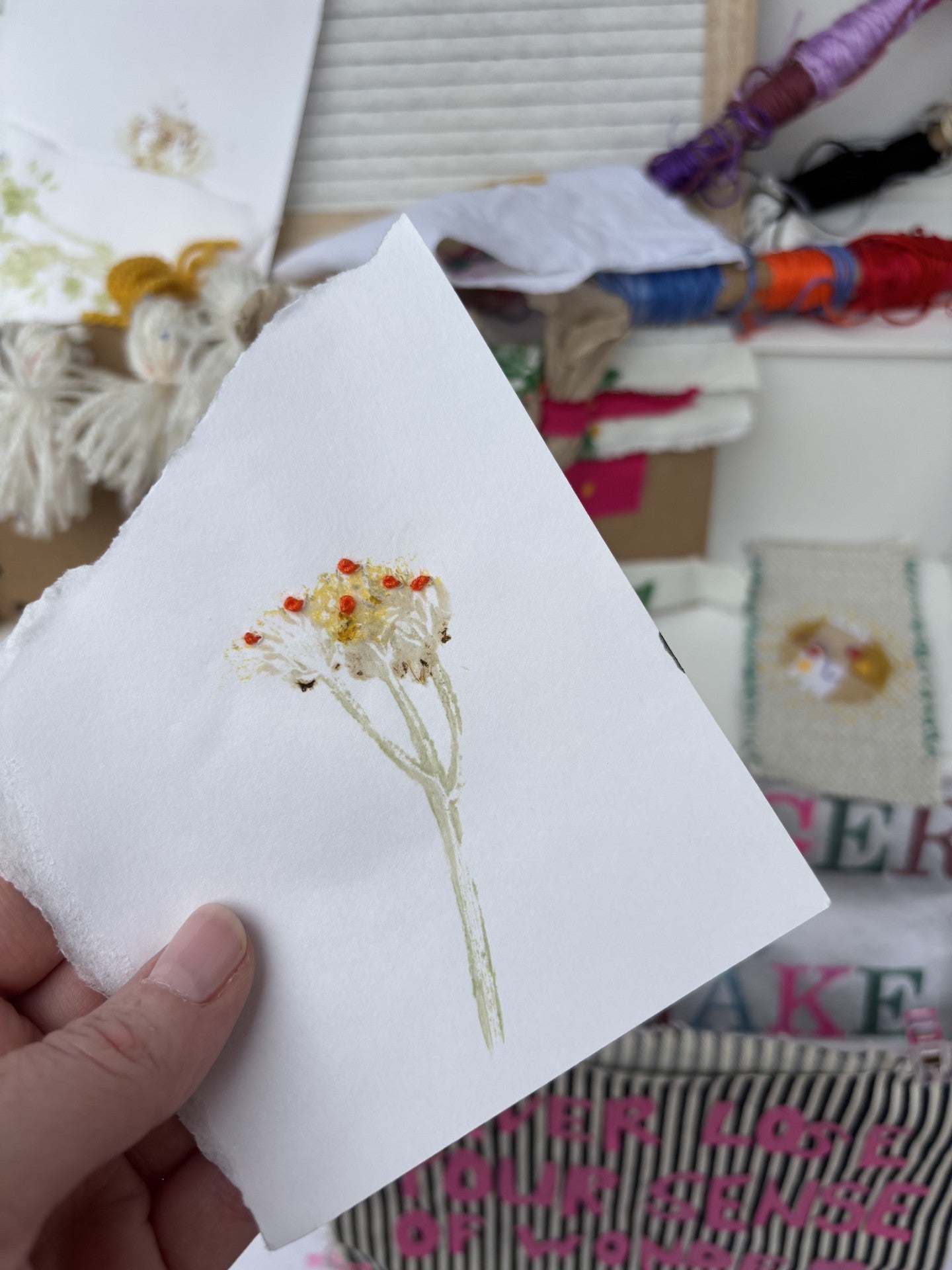 Embroidered flower design on a white fabric held by a hand with a sewing background.