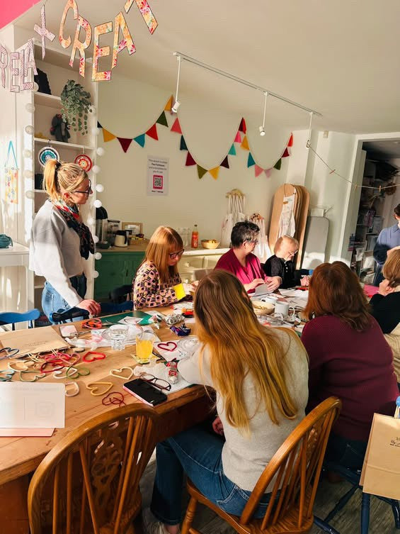 Group of people sitting around a craft table in a room with 'CREATE' decorations.