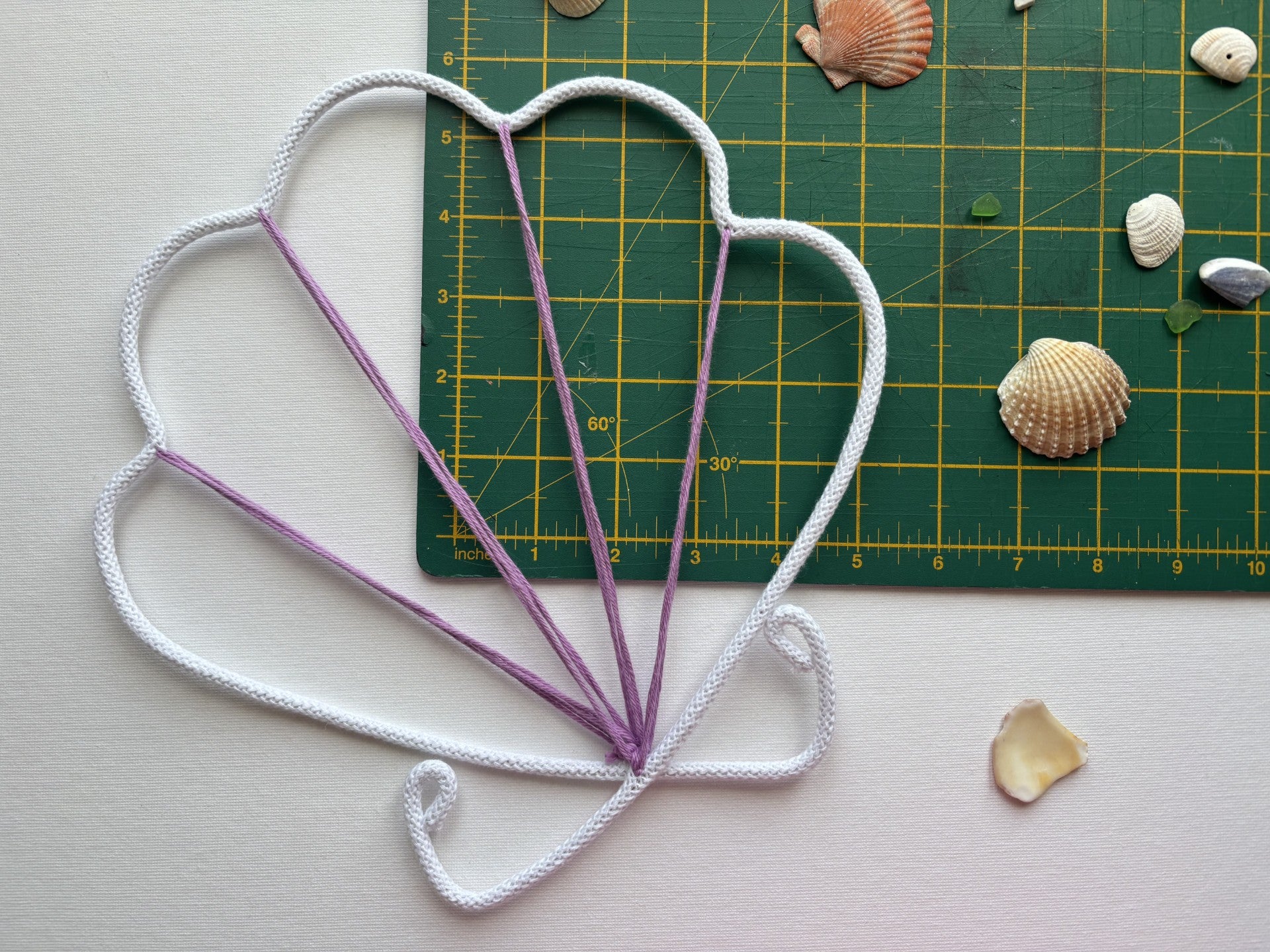 Wire shell in white and purple on a cutting mat with seashells.