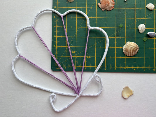 Wire shell in white and purple on a cutting mat with seashells.