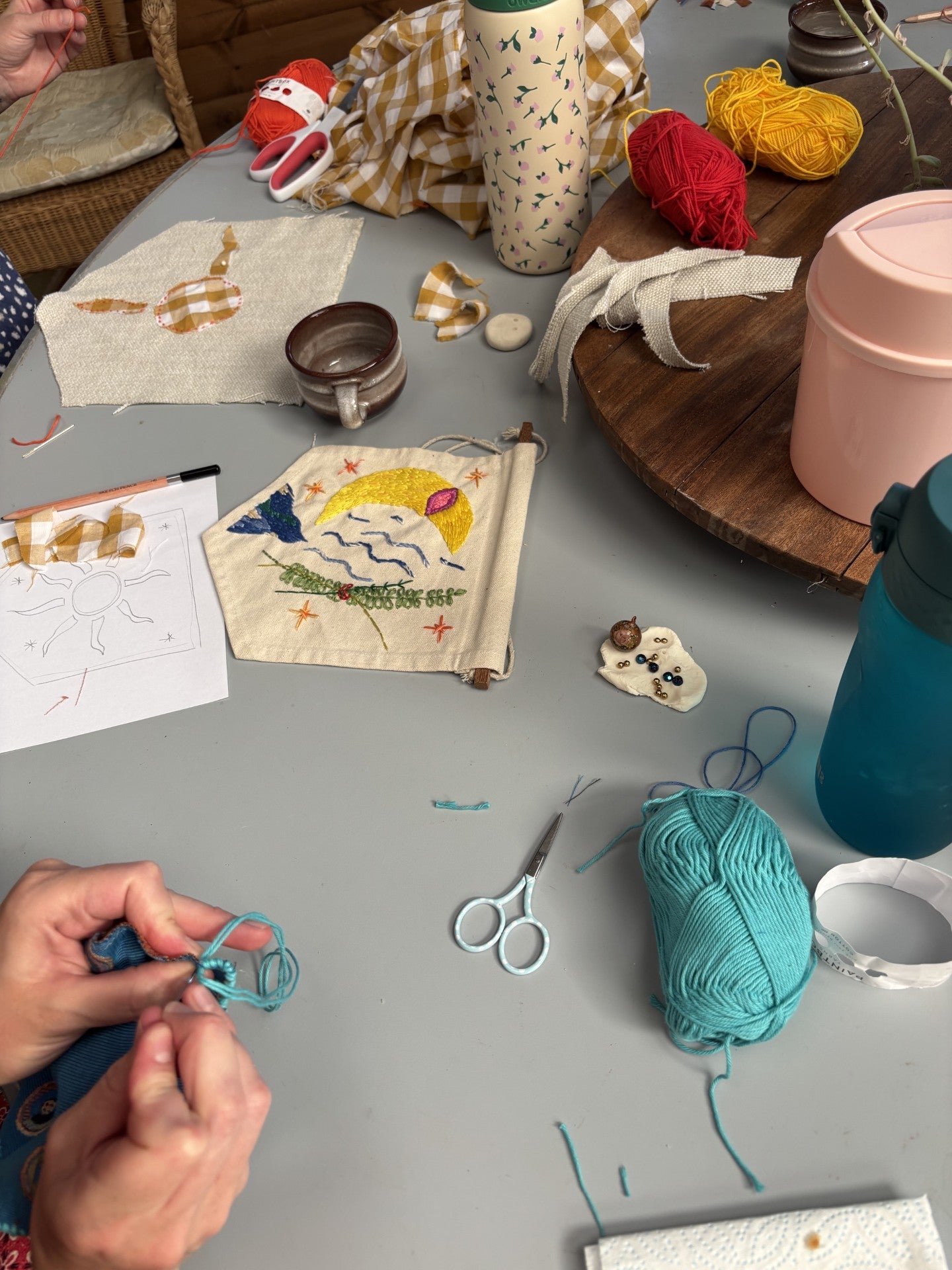 Table with embroidery materials, yarn, and a person working on an embroidery project.