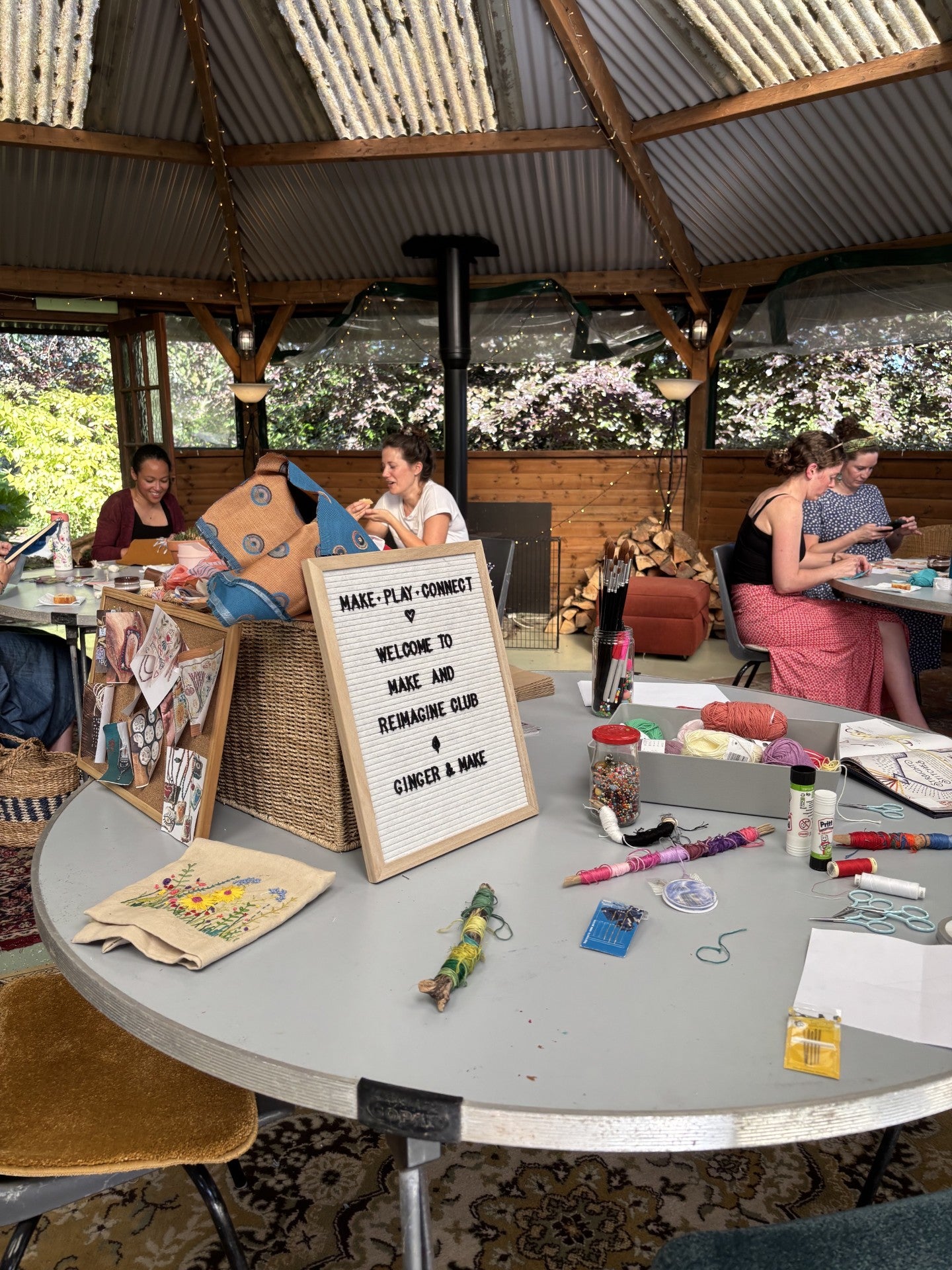 People sitting at a table with craft supplies and a sign in an outdoor setting.