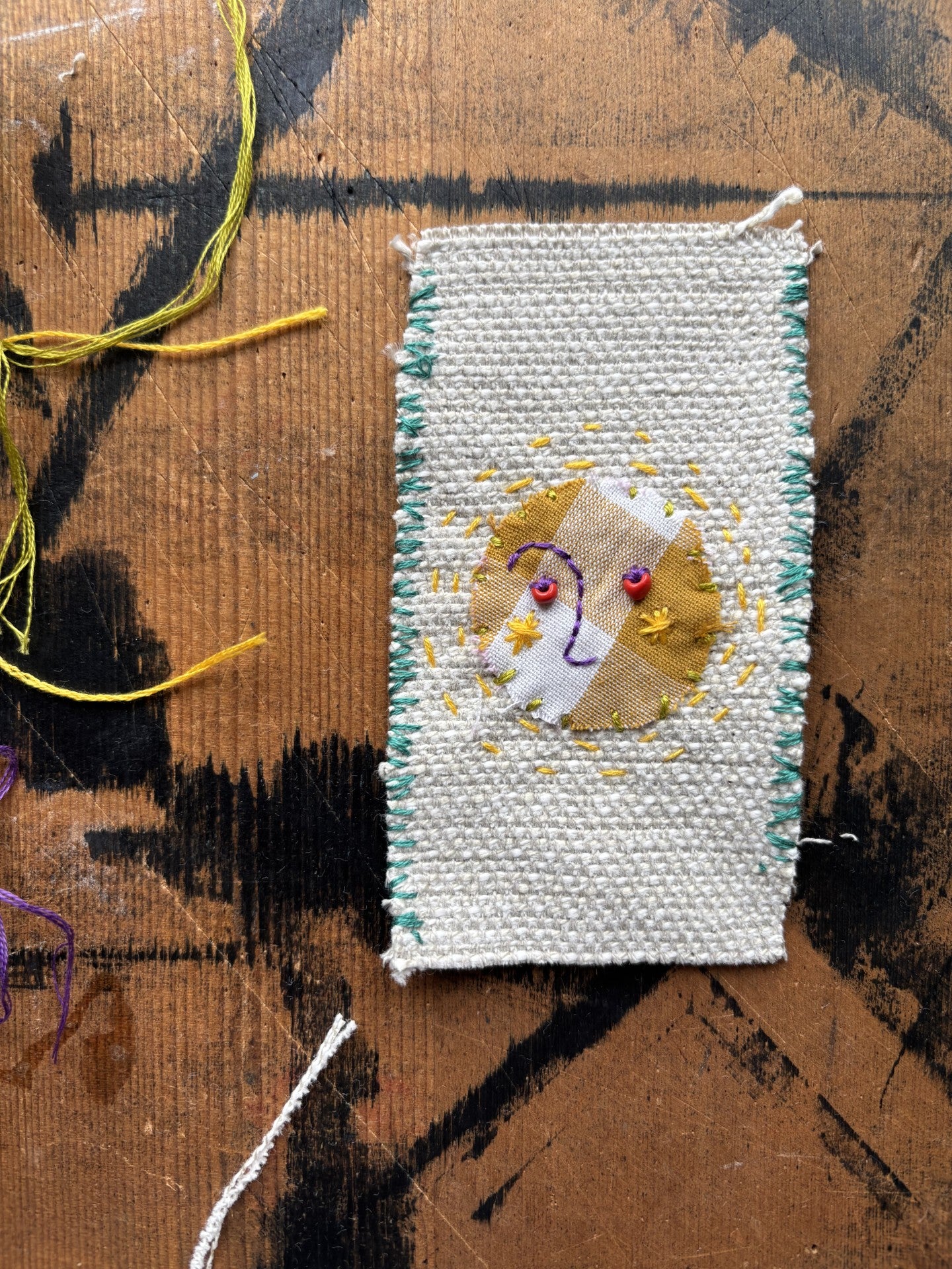 Handmade embroidered talisman with a sun design on a textured surface