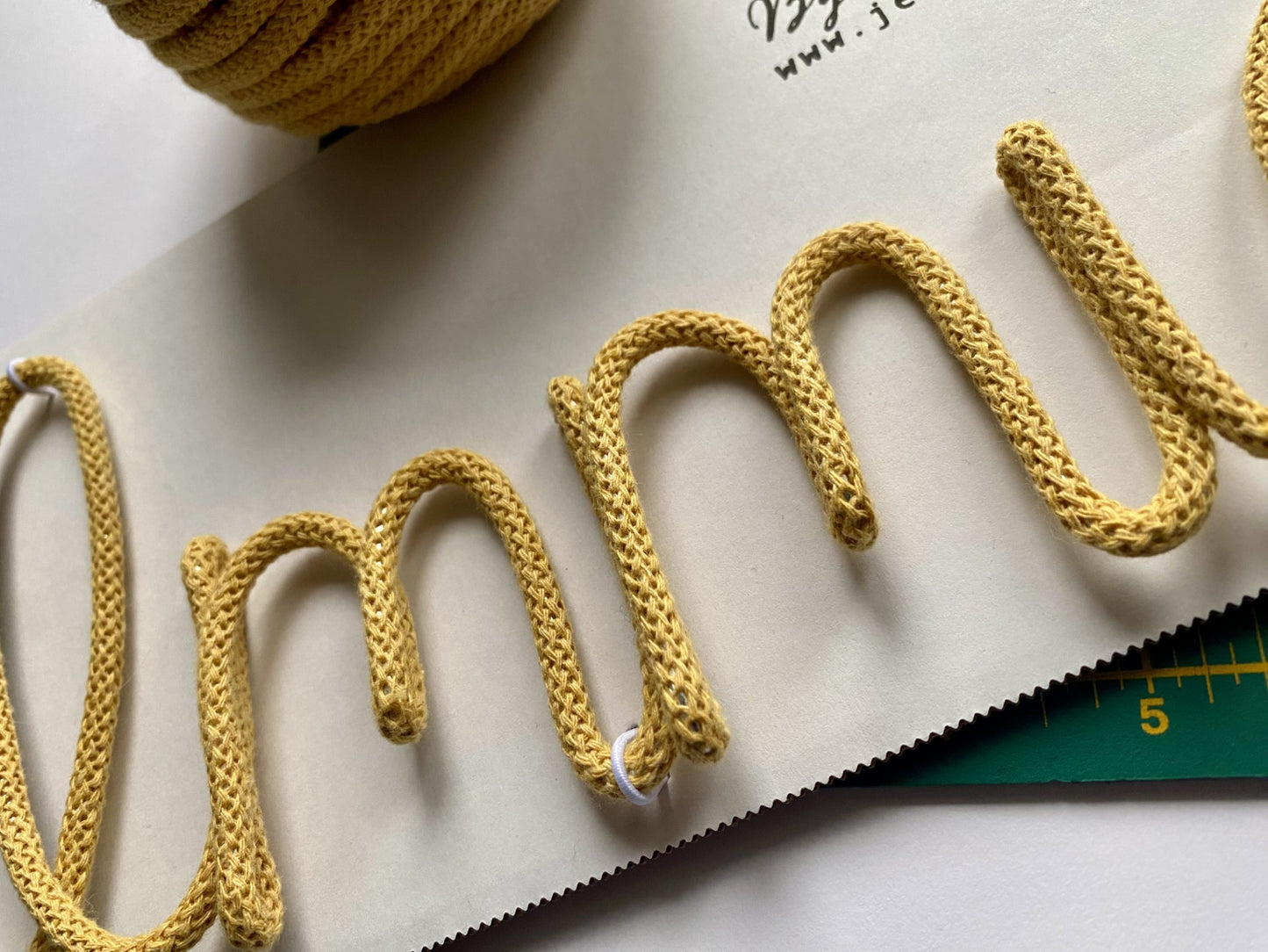 Honey knitted wire writing close up with a cutting mat for scale on a light background