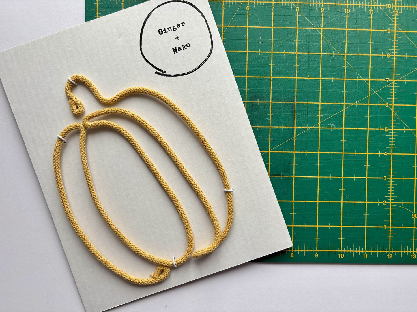 Honey yellow wire pumpkin on card with 'Ginger + Make' branding, placed on a green cutting mat.