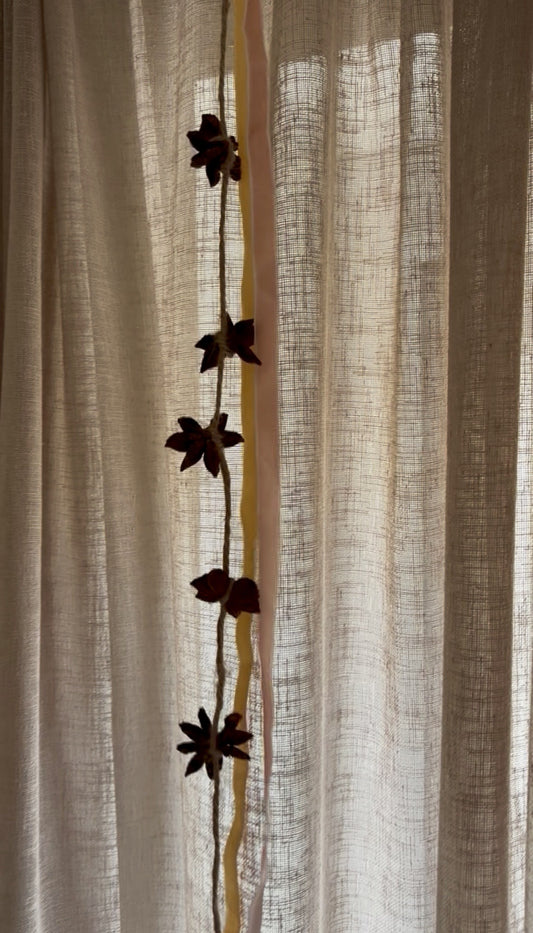 A close-up of a cream-colored linen curtain panel with a vertical decorative garland featuring dark brown flower silhouettes and a thin gold vertical stripe.