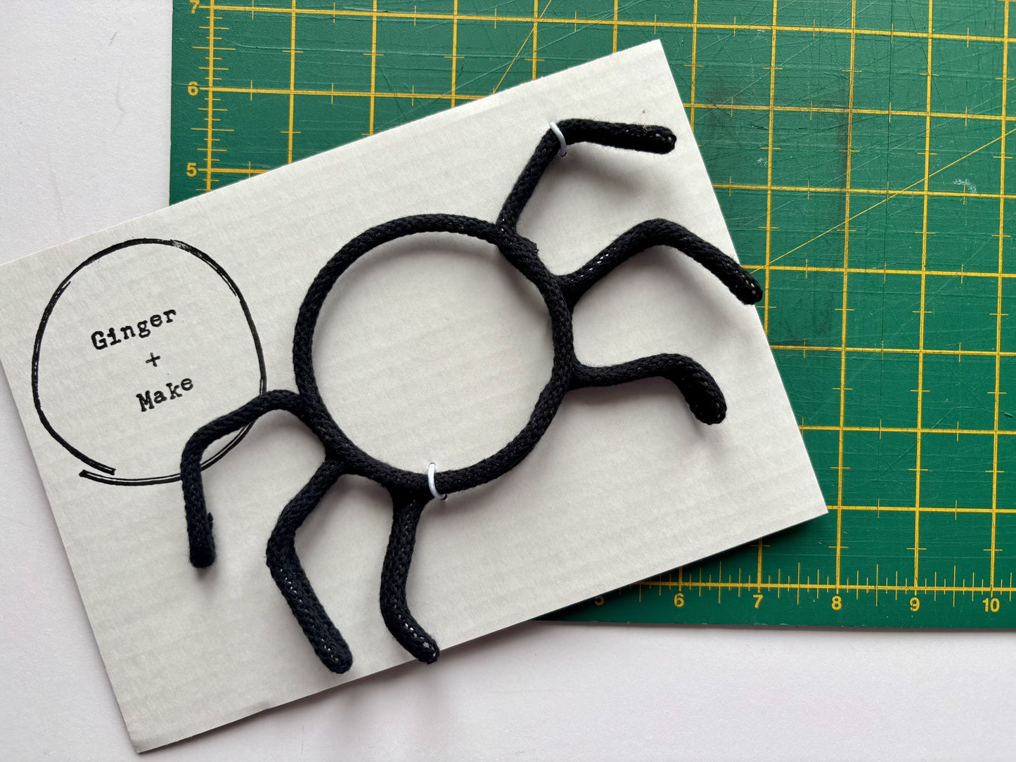 Black wire spider on white card with 'Ginger & Make' branding, placed on a green cutting mat.