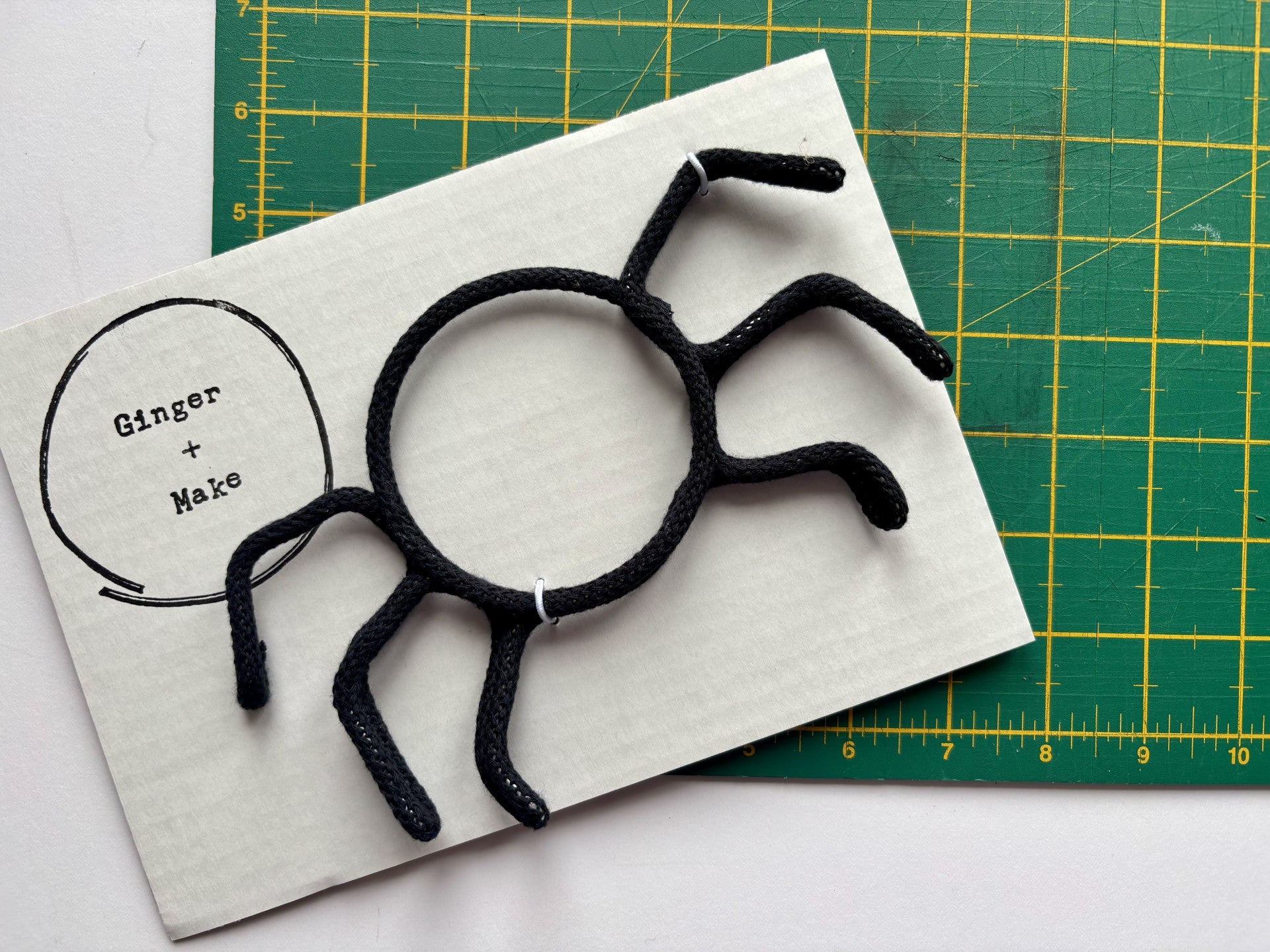 Black wire spider on white card with 'Ginger & Make' branding, placed on a green cutting mat.