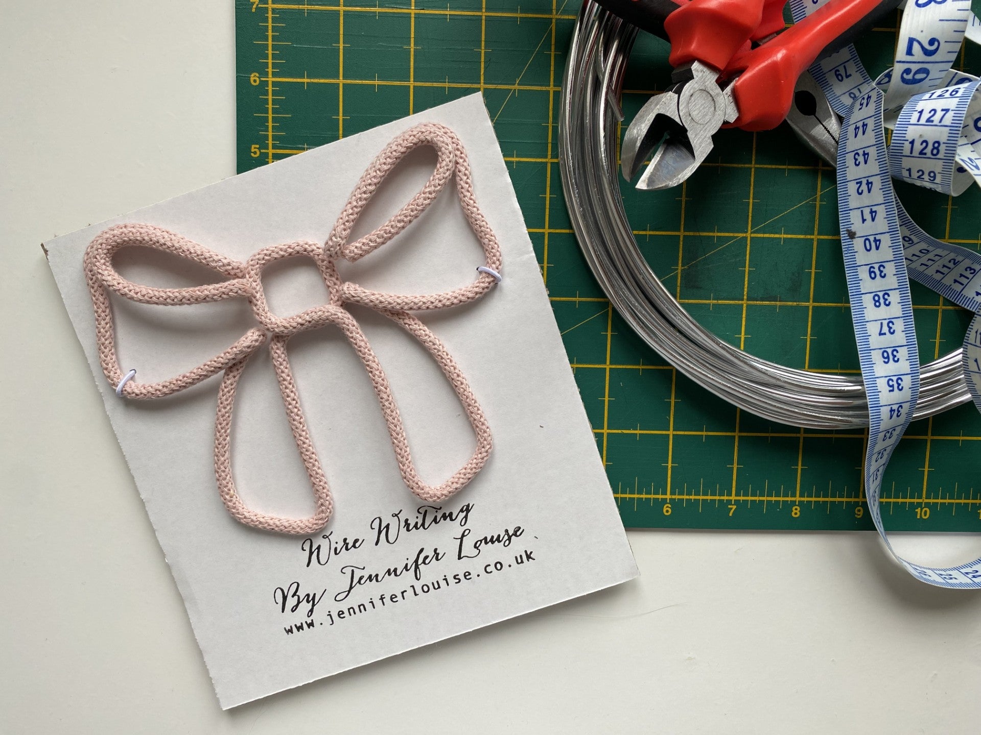 Pink wire bow on a card with tools on a green cutting mat