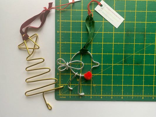 Decorative wire Christmas tree and bow with red pom-pom on a green cutting mat.