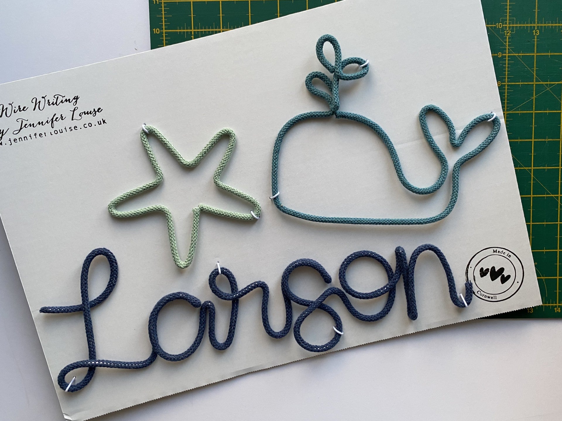 Personalised wire name with whale, starfish, and 'Larson' design on a white card.