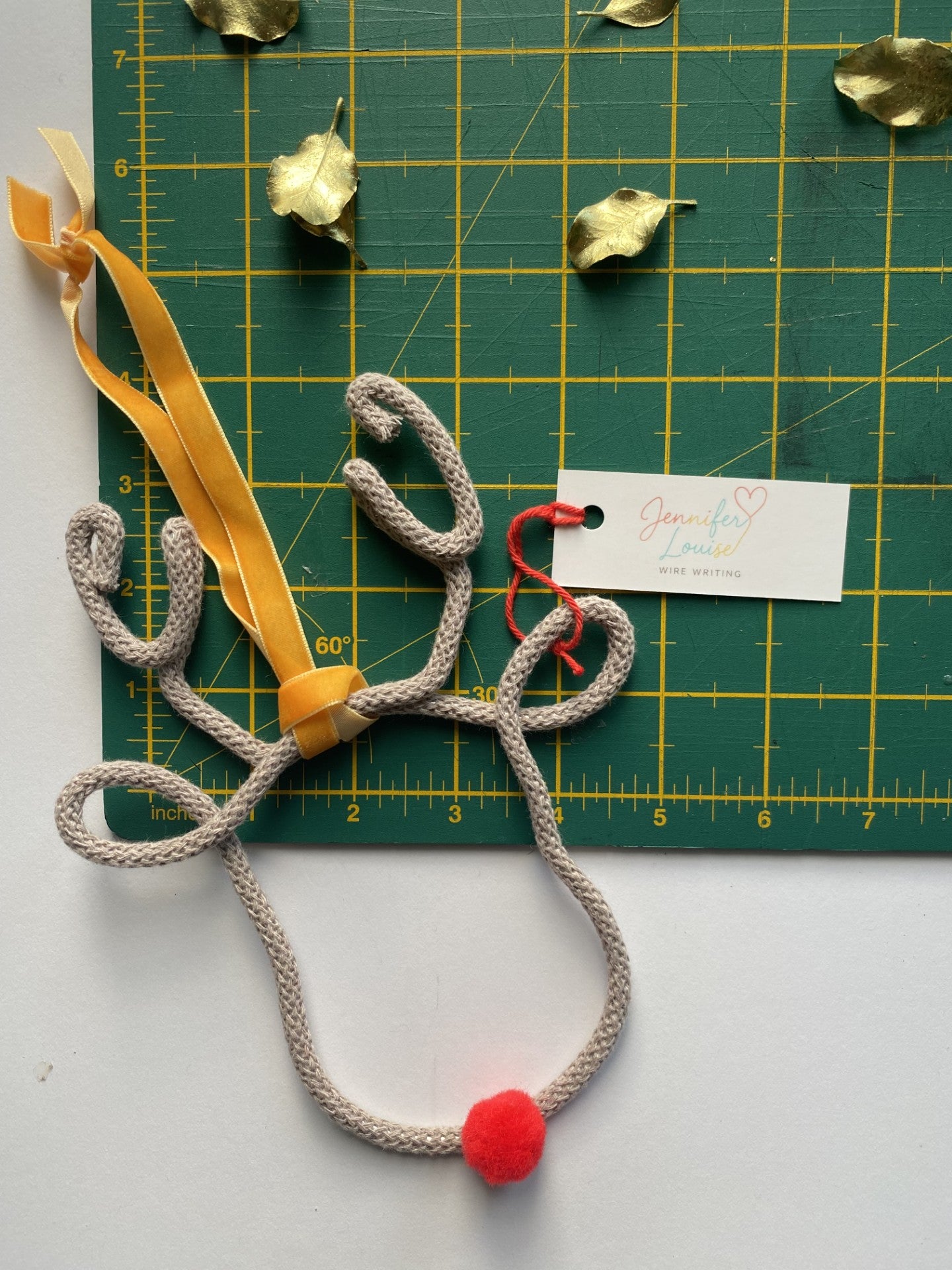 Decorative reindeer made from wire and ribbon on a green cutting mat with a brand tag.