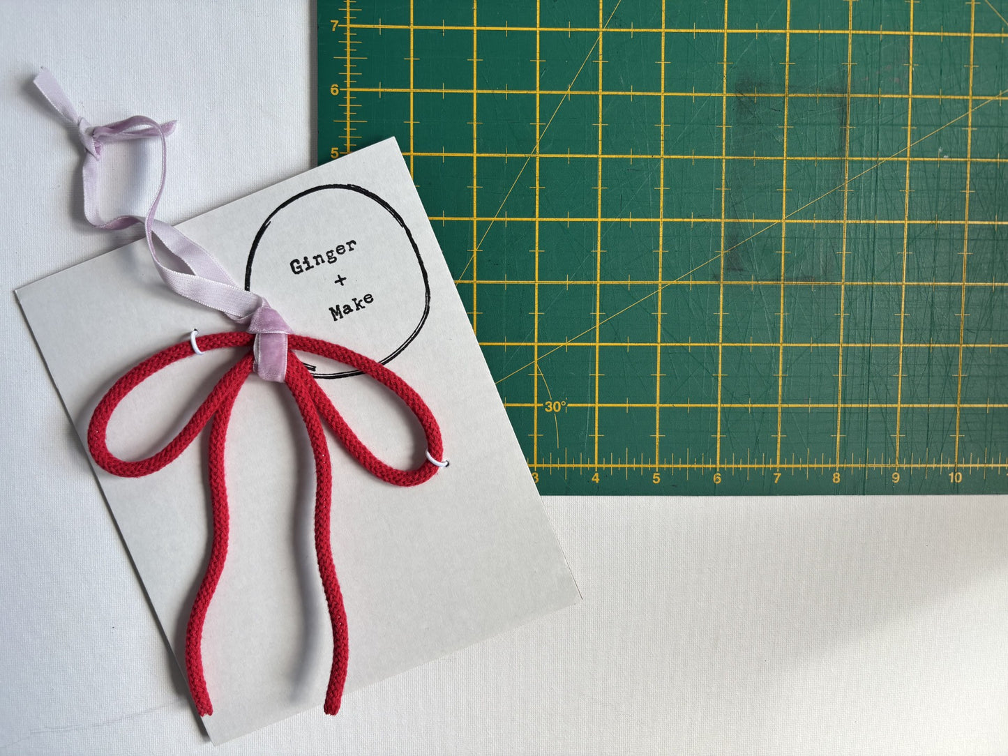 A wire bow with red cord, placed on a white surface next to a green cutting mat.
