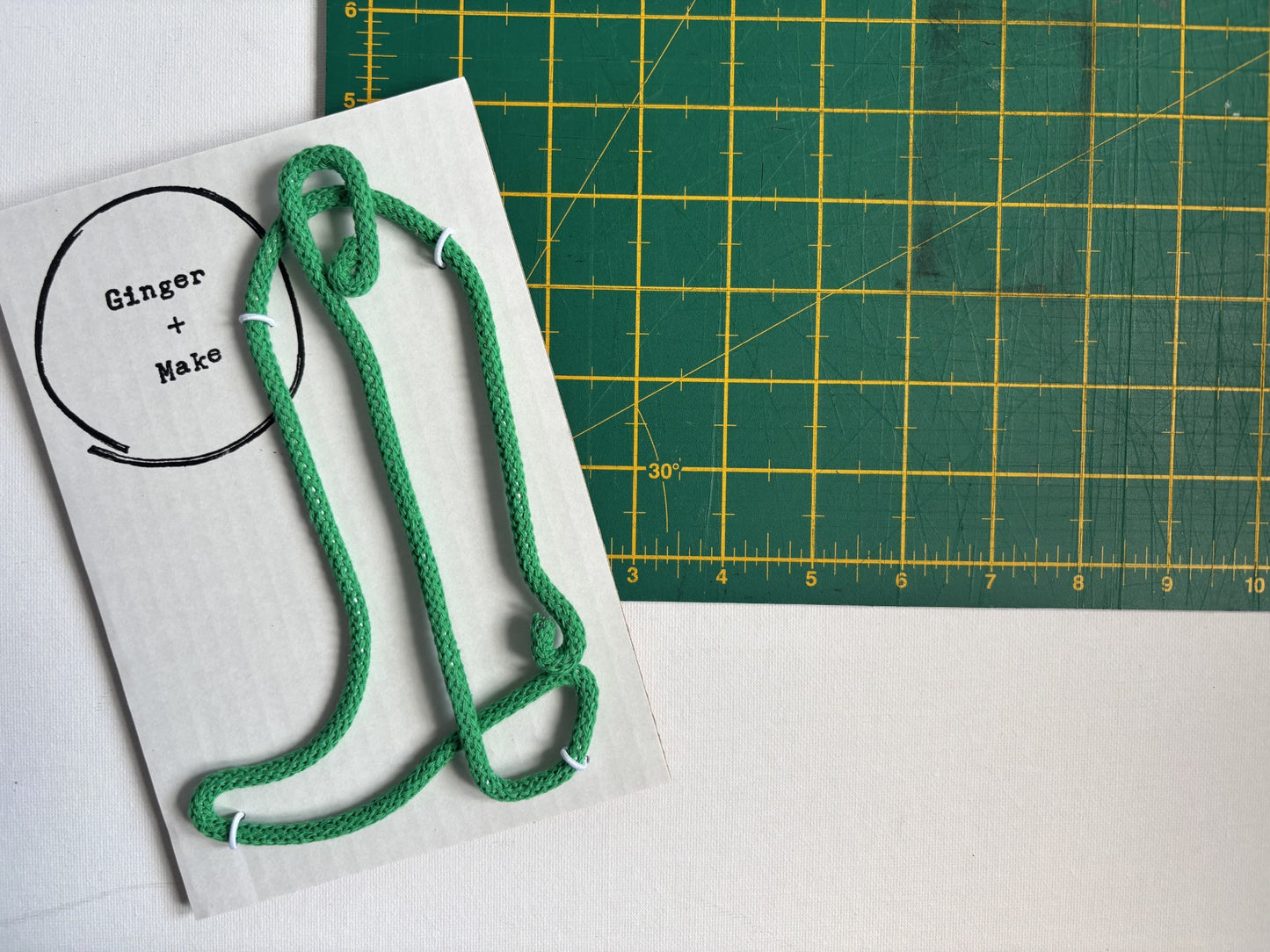 A green wire cowboy boot  laid on  white card next to a green cutting mat with yellow grid lines.