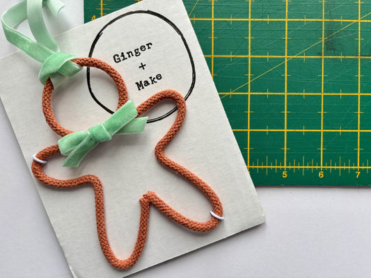 Orange wire gingerbread with green bow tie on a card, with 'Ginger & Make' branding, against a green cutting mat background.