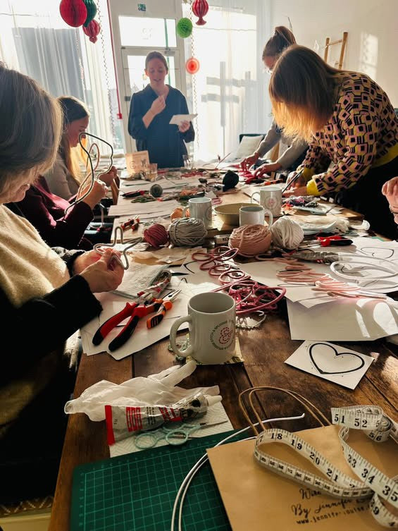 Group of people engaged in a craft or activity at a table with various materials and tools.
