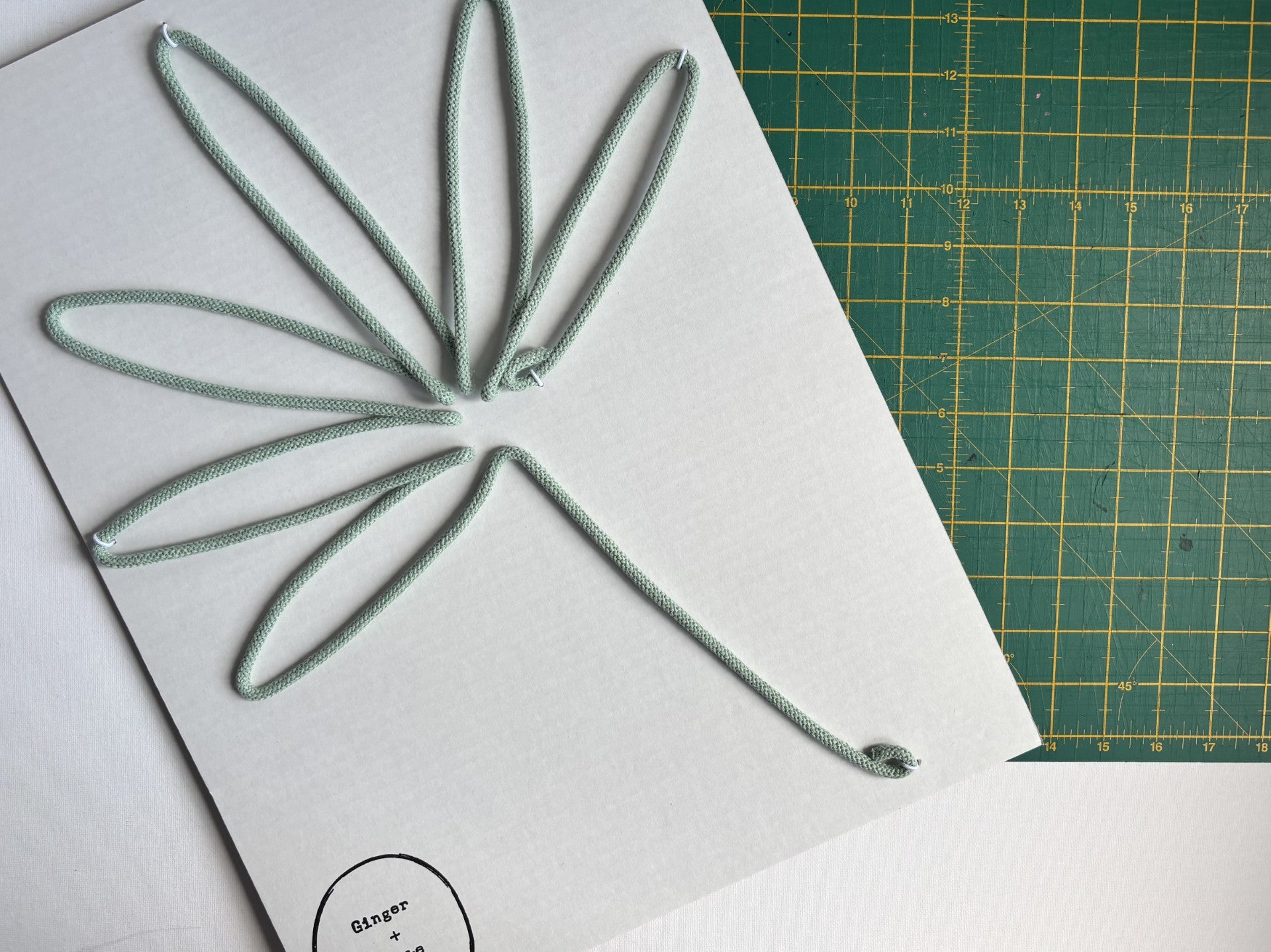 An Aloe Green wire palm leaf, placed over a green cutting mat with grid.